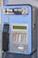 An old blue telephone booth damaged and out of service with signs of deterioration and some banditry painted on it