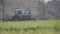 Old blue tractor riding along green grass on sunny spring day. Wide shot of agricultural engineering vehicle cultivating