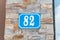 Old blue vintage house address metal plate number 82 on the decorative brick facade of residential building exterior wall on the s