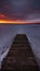 An old boardwalk pier on a large frozen lake with a dramatic evening sky and sunset crimson over the horizon