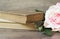 Old books and flower rose on a wooden background. Romantic floral frame background. Picture of a flowers lying on an antique book