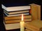 Old books stacked in a pile and a burning candle.