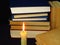 Old books stacked in a pile and a burning candle. Education, knowledge, reading habits, paper, library, light, flame, mystery