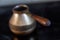 Old Bronze Turkish retro coffee maker kanaka on glass hob and stove with wooden handle, worn on a black background in an apartment