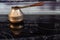 Old Bronze Turkish retro coffee maker kanaka on glass hob and stove with wooden handle, worn on a black background in an apartment