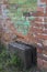 Old, brown, covered with web suitcase near a dirty brick wall so