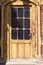 Old brown peeling door. There are black panels on the door. The sun is shining on the door