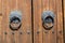 Old brown wooden massive gate, closed door, double entrance with handmade iron handles and knockers