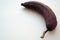 Old brownish-brown darkened banana in a skin. On a white textured background