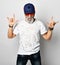 Old brutal man in designer t-shirt, blue jeans and baseball cap shows rock with both hands stylish fashionable men