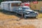 Old Buick sedan hitched to caravan parked and left besideprivate property sign with signs of known brands on fence