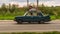 Old car Lada 2106 rides on a rural highway. Green vintage sedan motor car with wheelbarrow on the roof rushes on the country road