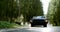 Old classic car is moving on countryside road in forest in daytime, frontal view from ground