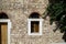 Old classic little church arch window and door frame on earth tone natural stone wall facade background with green tree leaves