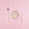 Old clock, knife and fork on pink background. Minimal composition. Copy space