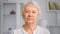 Old company lady manager with short hair looks straight standing against blurred white bookshelves