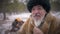 Old confident indigenous man stroking grey beard looking away smiling. Portrait of senior man sitting in winter forest