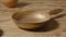 An old copper frying pan with a handle on a rustic wooden table next to an clay jug. Gold round empty skillet, stainless