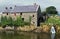 The Old Corn Mill at Annalong Harbour bathed in full sunshine while the Mountains of Mourne behind are shrouded in thick cloud