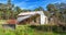 Old damaged cottage surrounded by Eucalyptus trees under a blue cloudy sky in Adelaide Hills