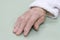 Old damaged leather of a very old woman`s hand in a white bathrobe on a light background.