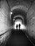 Old dark pedestrian tunnel with two unrecognisable people in silhouette against white light walking forwards