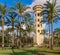 Old decorated antique elevated water tank framed by high palm trees before sunset with partly cloudy blue sky