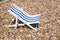 Old decoration toy striped beach chair for sunbathing and relaxing stands on a stones beach in a warm sunny day