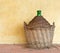 Old demijohn aka carboy for wine, wicker straw basket. by house. Y