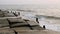 Old destroyed concrete embankment with wooden pillars protruding from the water against the background of ocean waves in the eveni