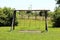 Old dilapidated wooden retro vintage outdoor public playground equipment in shape of swing with two seats surrounded with grass