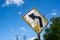 Old, dilapidated yellow curve ahead road sign with peeling paint against blue sky with power lines