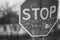 Old dirty bent road stop sign close-up, blurred rural house in the background. Black and white photo