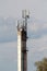 Old dirty concrete industrial chimney with rusted metal steps and cell phone antennas on cloudy sky background