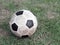 old dirty stained soccer ball made of synthetic rubber on green grass field