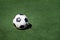 Old, dirty tattered soccer ball on background of green grass. Traditional classic black and white football ball on green