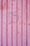 An old distressed wooden vertical plank texture with dry peeling pink paint