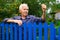 Old elderly farmer stands at fence of his country house and threatens someone with his fist