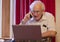 Old elderly senior man on phone at laptop computer at risk to cyber attack and online bank fraud