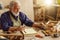 Old experienced carpenter sitting at the messy table at workplace