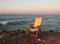 An old fading empty wooden chair in reflected sunset light left next to the sea on a calm summer evening