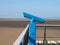 Old fashioned blue telescope on the end of southport pier in merseyside with a sunlit summer beach and blue sky