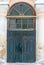 The old-fashioned dark green door with the window element above on the background of the unrestored wall in monastery