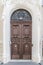 Old fashioned front door entrance, all in dark brown colors. Beautiful stone door platband and metal transom