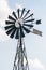 Old-fashioned metal wind pump against pale blue sky with white clouds