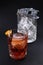 Old fashioned Negroni cocktail near glass with ice on the black background