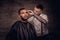 Old-fashioned professional tattooed hairdresser does a haircut to an African American client. Isolated on dark textured