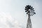 Old-fashioned wind powered water pump against pale blue sky with clouds