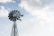 Old-fashioned wind powered water pump against pale blue sky with clouds