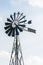 Old-fashioned wind powered water pump against pale blue sky with white clouds